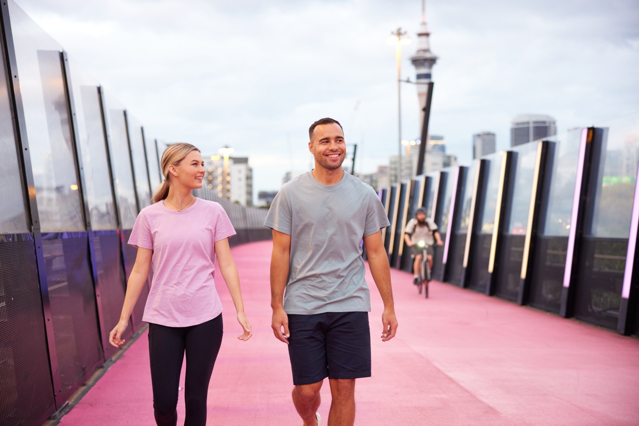 Two people walk along the pink path with Auckland city in background